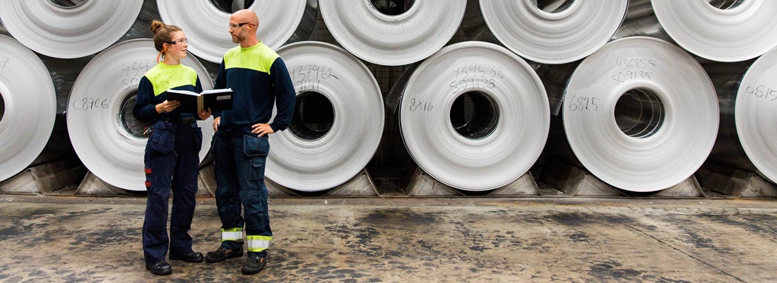 Two employees in front of stacked aluminium coils.